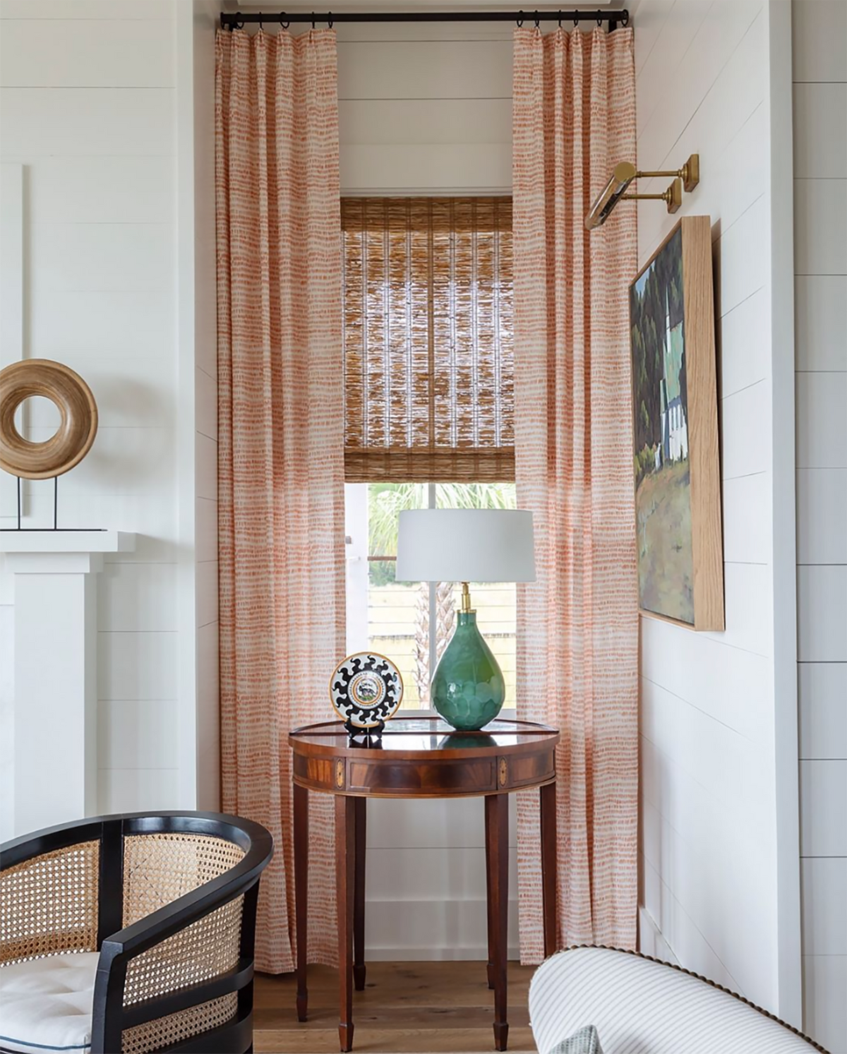 A corner of a living room with a window. There are curtains in Dashes in Tangerine, a small scale print. There is a table with a lamp in front of the window. A chair is partially in the frame. Allison Elebash is the interior designer.