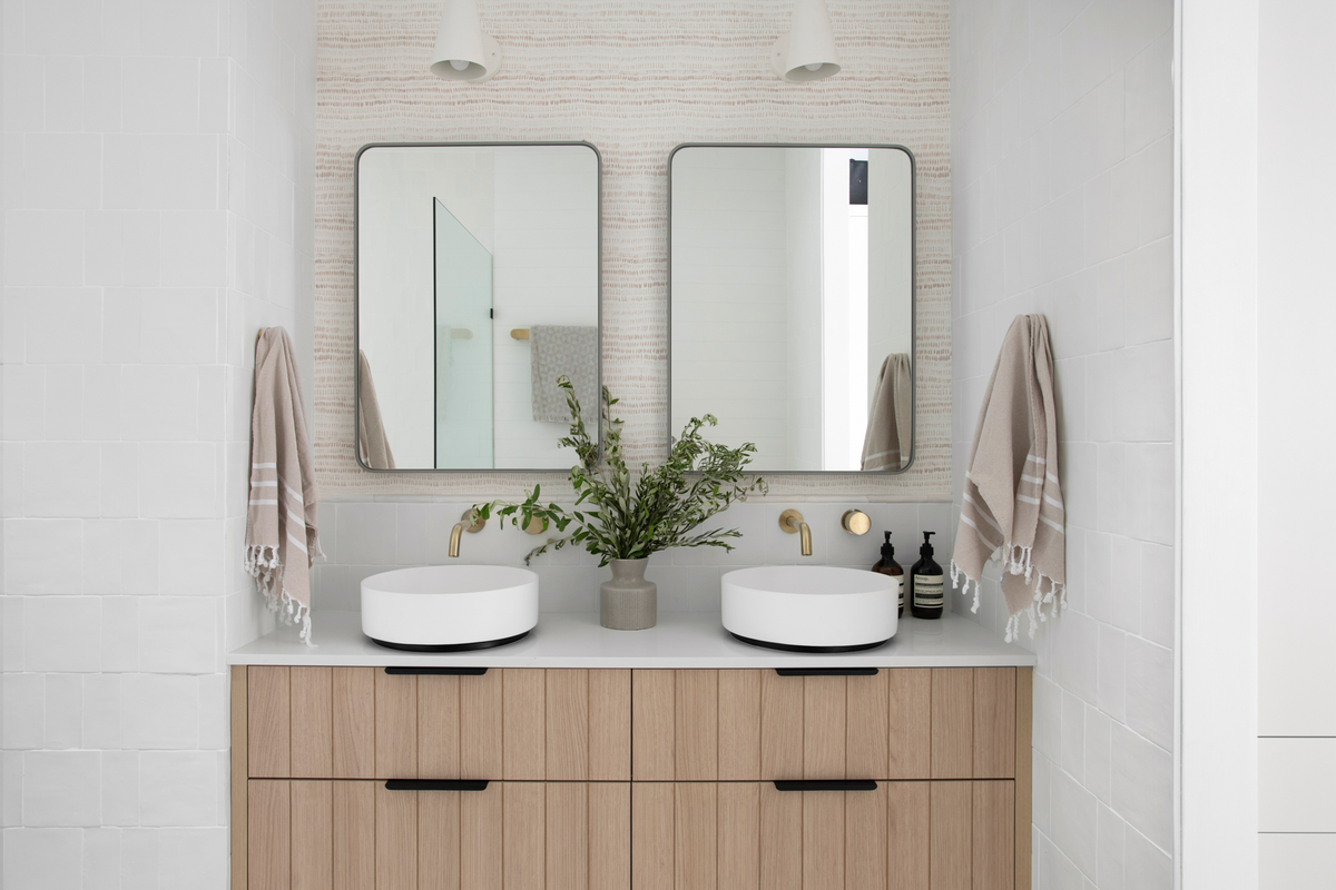 A bathroom vanity with two sinks and two rectangular mirrors. The Dashes wallpaper is on the wall behind the mirrors. It's a small scale pattern in taupe that reads as a texture.