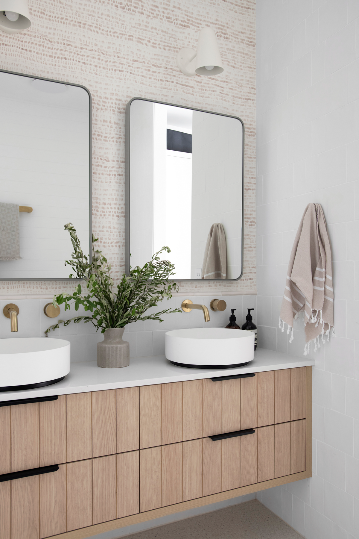 A bathroom vanity with two sinks and two rectangular mirrors. The Dashes wallpaper is on the wall behind the mirrors. It's a small scale pattern in taupe that reads as a texture.