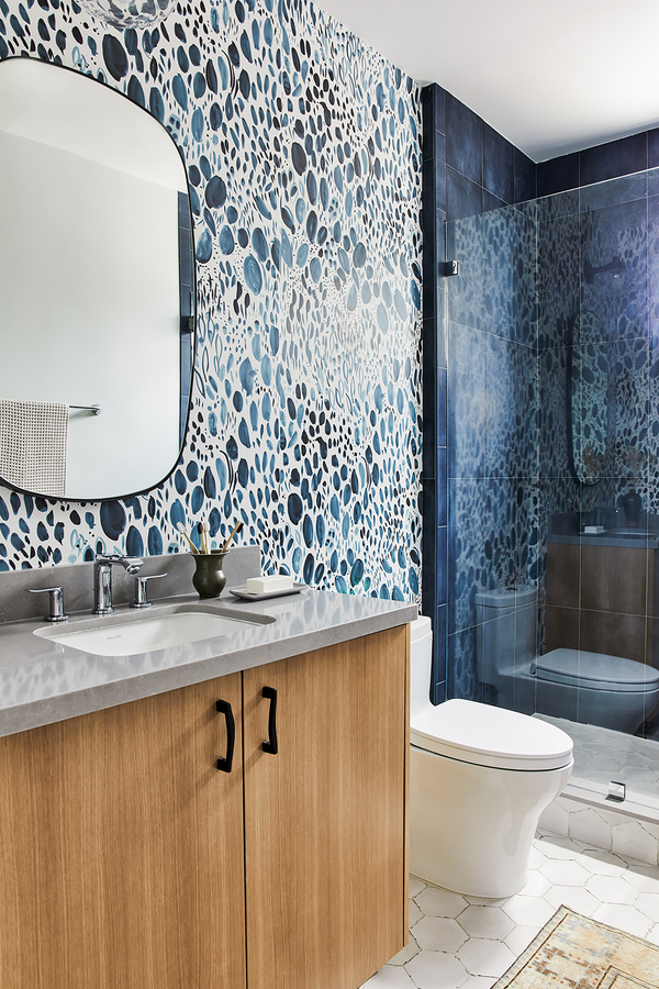 A small bathroom with wallpaper in our Blooms pattern in navy. The pattern is made up of loose painterly marks that reference a garden. There is a sink in the foreground with a wooden cabinet underneath and a mirror above.