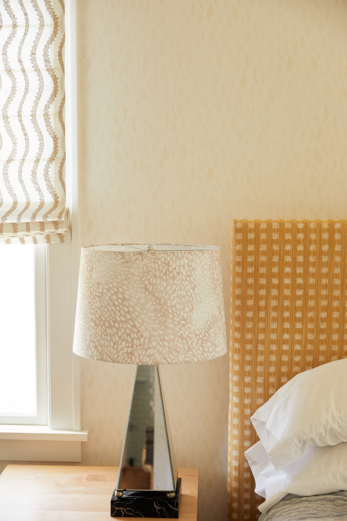 Notched Vines Roman Shade in Ivory/Gray, Petals Wallpaper in Shell, Speckled Lampshade in Taupe/Fawn, and Gridded Ikat Headboard in Goldenrod