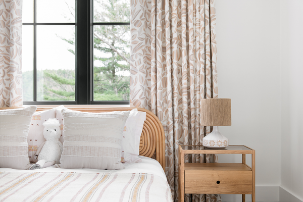 A bedroom with a bed against a white wall with curtains in our Striped Garden fabric. The pattern is tonal taupe colors and garden shapes.