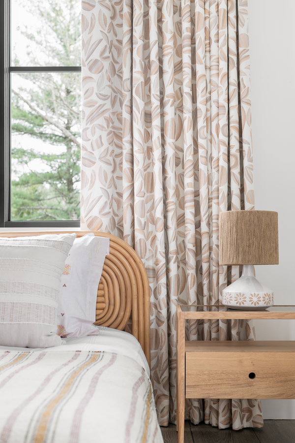 A bedroom with a bed against a white wall with curtains in our Striped Garden fabric. The pattern is tonal taupe colors and garden shapes.